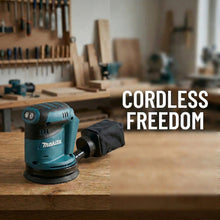Makita DBO180Z cordless sander lifestyle in natural woodworking environment, blue body